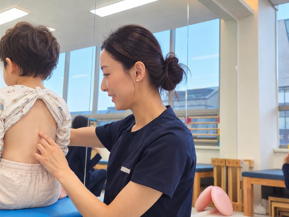 열매아동발달연구소 위례점 치료실에서 선생님이 아이의 척추와 등 근육 균형을 살펴보는 자세교정재활 모습